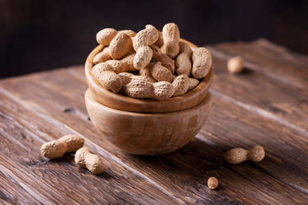 Roasted peanuts in wooden bowl on dark background, selective focus image