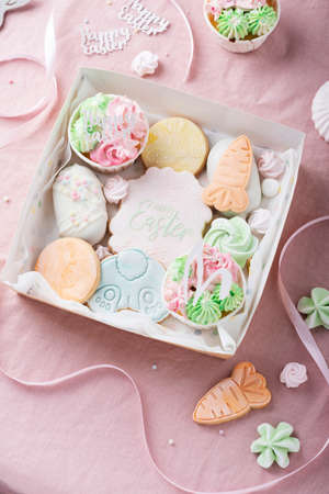 Mix of Easter cookies in the paper box on the pink table, selective focus image