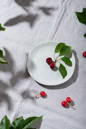 Summer concept with hard sun light, red cherry with leaves on the grey tableclolth, selective focus imageの写真素材