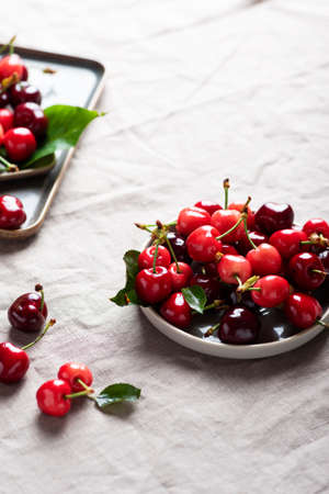 Fresh sweet cherry with green leaves on the linen tablecloth, selective focus image