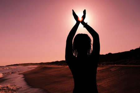 Silhouette of a woman on the beach holding the sun between her fingersの写真素材