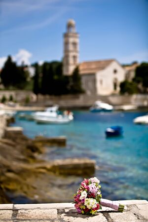 Colorful bouquet on the edge of a Mediterranean pier with a church and some boats in the background.の写真素材