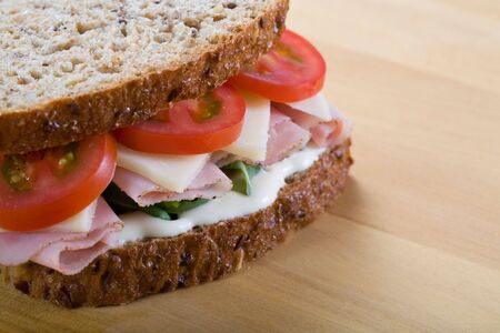 Healthy ham, cheese, tomato, rocket and mayo sandwich on a bread board.の写真素材