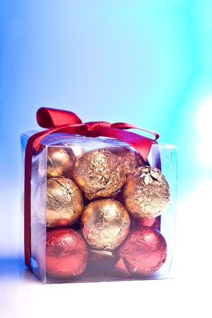 A clear box with gold and red chocolate balls inside it and a red ribbon around itの写真素材