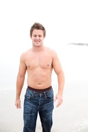 A Attractive topless man on the beach looking down and smilingの写真素材