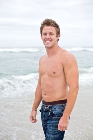 An attractive topless man looking towards camera smiling on the beach.の写真素材