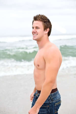 An attractive topless man looking off into the distance on the beachの写真素材