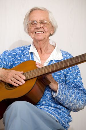 Elderly woman playing the guitar wearing a blue knitted top.の写真素材