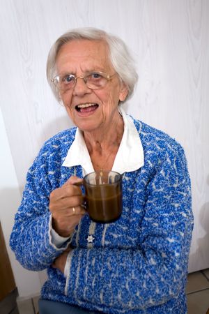 Happy old woman holding a cup of coffee while smiling.の写真素材