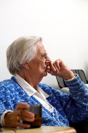 Elderly woman witting with a coffee in one hand and her other hand over her lips.の写真素材