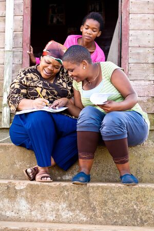 Two black woman filling out a form while sitting on steps and a young black girl stairing over their shoulders.の写真素材