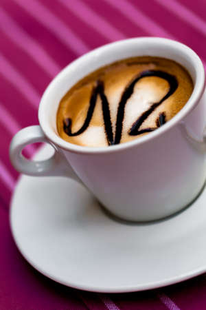 Small white cup of coffee with a pink, stripe table cloth.の写真素材