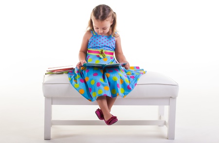 The little girl is sitting on the bench reading her books の写真素材