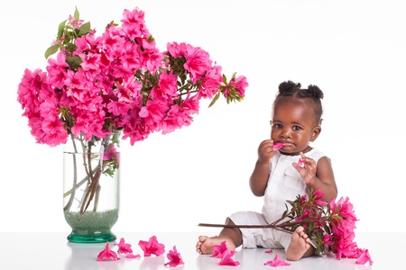 Black baby girl eating a pink flower.の写真素材