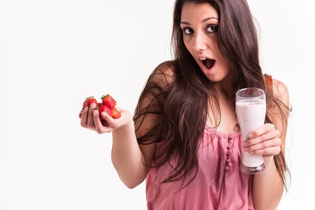 A young female model with strawberries in the one hand and strawberry smoothie in the other の写真素材