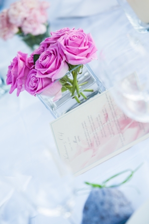 Pink roses in a glass vase with the menu on a table.の写真素材