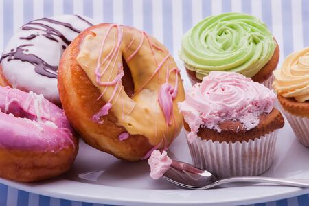 A white plate filled with dougnuts and cupcakes of all coloursの写真素材