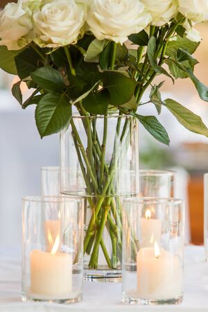 A whole bunch of roses in a pot on a table with candles.の写真素材