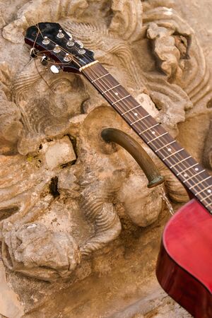 A red guitar standing by a wall tap with water dripping.の写真素材