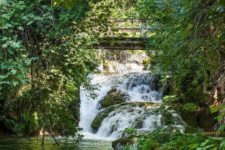 A small waterfall is running over the rocks under a bridge.の写真素材