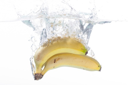 Three bananas being cleaned in a bowl of water.の写真素材