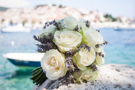 A beautiful bouquet of white roses laying on a rock by the ocean.の写真素材