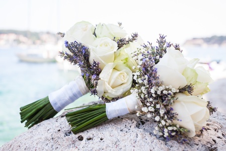 A beautiful bouquet of white roses laying on a rock by the ocean.の写真素材