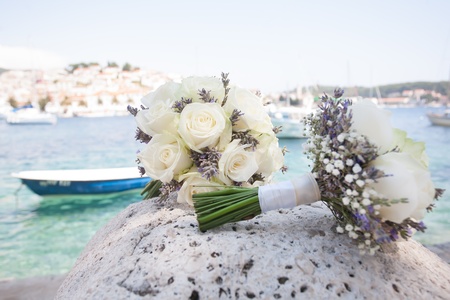 A beautiful bouquet of white roses laying on a rock by the ocean.の写真素材