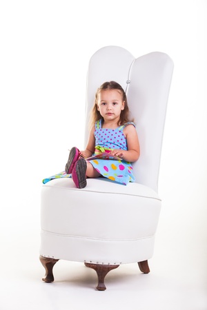 Little girl sitting on a big chair, busy with her books.の写真素材