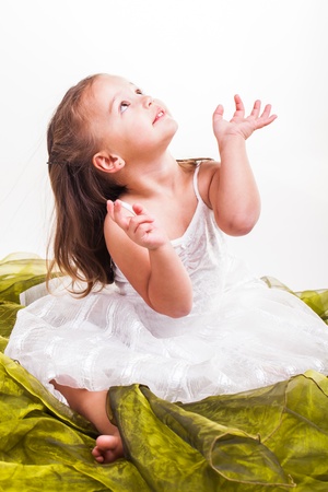 A little girl sitting on a piece of green organza.の写真素材