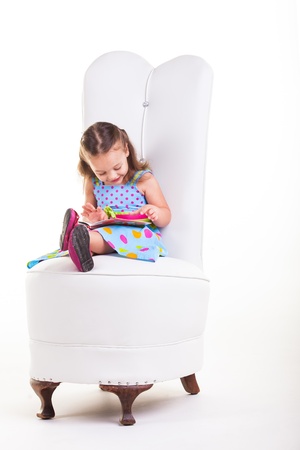 A little girl sitting on a big chair reading her book.の写真素材