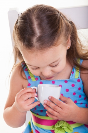 A little girl sitting on a big chair drinking her cup of coffee.の写真素材