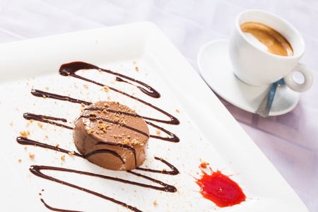 A plate of mousse filled with chocolate sauce and a drop of red jam with coffee..の写真素材