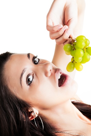 a beautiful young caucasian girl with brunette hair and dark eyes seductively eating fresh green grapesの写真素材