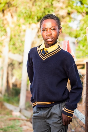 an teenage african boy readily dressed in his school clothes waiting by the fence before school startsの写真素材
