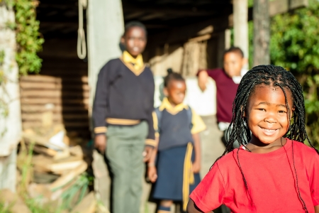 a pretty african girl with braided hair and a bright red shirt smiling confidently with her siblings in the backround watching over herの写真素材
