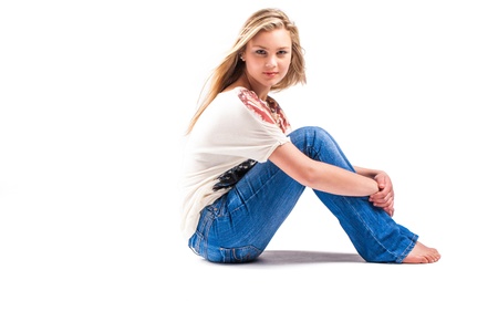 a pretty teenage caucasion girl with blond hair and blue eyes sitting in the studio with blue jeans and an american printed shirtの写真素材