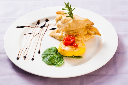 a colorful gourmet dish of chicken fillet in creamy cheese batter with a side portion of fried potato and cheese fritter and fresh spinach as garnishの写真素材