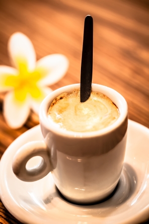 a close-up of a single manchiato stirred on a wooden table with a frangipani in the backroundの写真素材