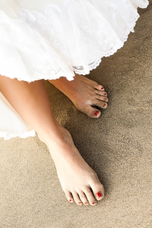 a close-up on a dress being lift up to reveal slim sandy feet with red toenailsの写真素材