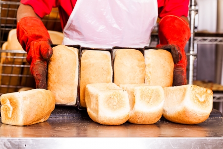 baker removing bread out of the bread pans in red heat-protection glovesの写真素材