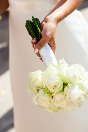 cropped image of a bride holding her beautiful white rose bouquet wrapped in white ribbonの写真素材