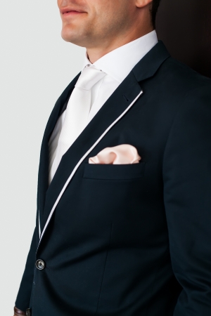cropped image of the groom in a dark navy suit with white piping and a crisp white shirt and tie with a peach  hankerchief peeping out of his pocketの写真素材