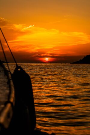 a beautiful golden sun setting on the horizon taken from a yacht with the buoy hanging off the edgeの写真素材