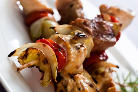 a close-up image of a portion of chicken kebabs grilled with onions and bell peppers for extra taste served on a white porelain plateの写真素材