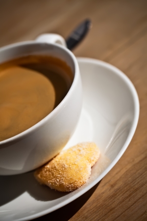 cropped image of a black americano coffee in a white porcelain cup served with a sugar coated heart bisquit on the saucer.の写真素材