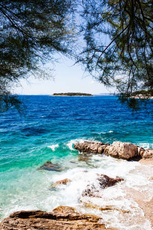 a small island spotted through the trees with clear aqua waves breaking on the rocky shore