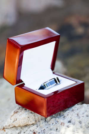 a close-up of the grooms black and silver alluminium wedding ring in a smooth wooden box resting on a rockの写真素材