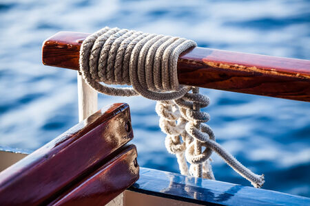 a close-up image of rope knotted to the hangle bar on the boat with the blue waters in the backgroundの写真素材