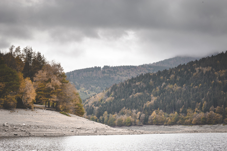 Lake Kruth-Wildestein in Vosges with low waterlevel and autumnal trees on mountains. dark moody skiesの写真素材